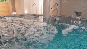 An indoor swimming pool with multiple water jets, tiled walls, and a wooden partition. - Hotel Spa Odeón (Naron)