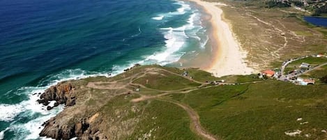 Vista aérea de una zona costera con playa, costa rocosa y un pequeño poblado con edificios y caminos.