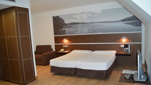 A bedroom with a bed, a chair, a wardrobe, a nightstand with a lamp, and a TV. - Hotel Spa Odeón (Naron)