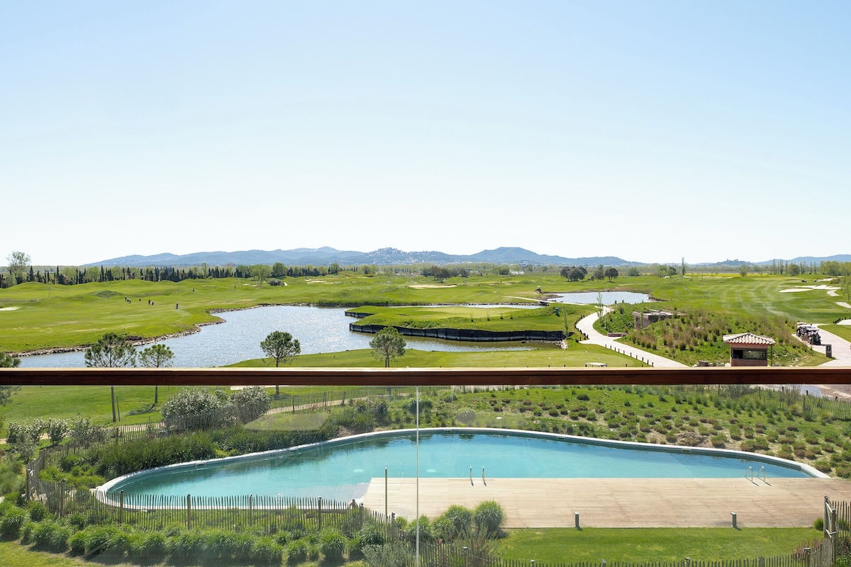 A pool with a view of a golf course and mountains in the distance.