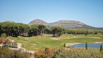 Un campo de golf con un lago, árboles y montañas al fondo.