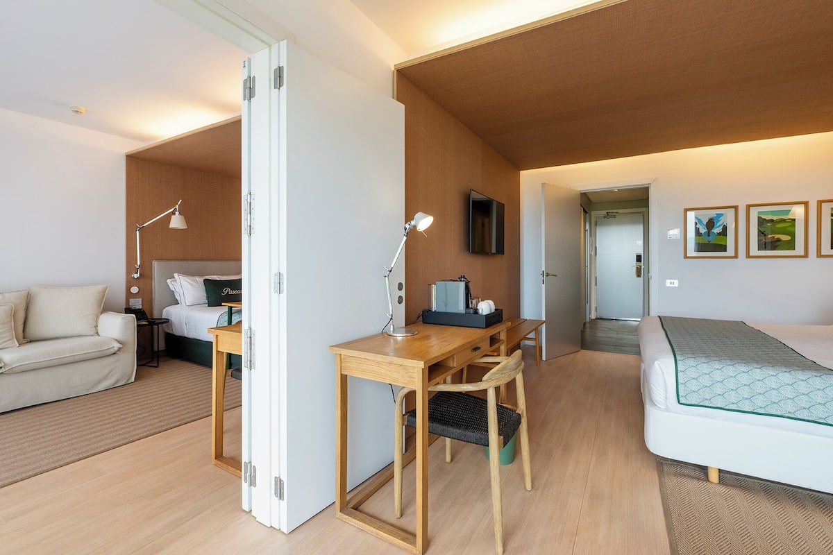 A modern hotel room with a bed, desk, chair, and a sofa.