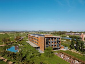 Um edifício moderno com piscina, rodeado por vegetação e um campo de golfe.