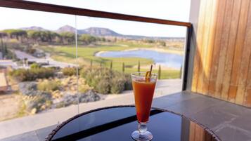 A glass of orange juice on a table with a view of a landscape including a lake and mountains.