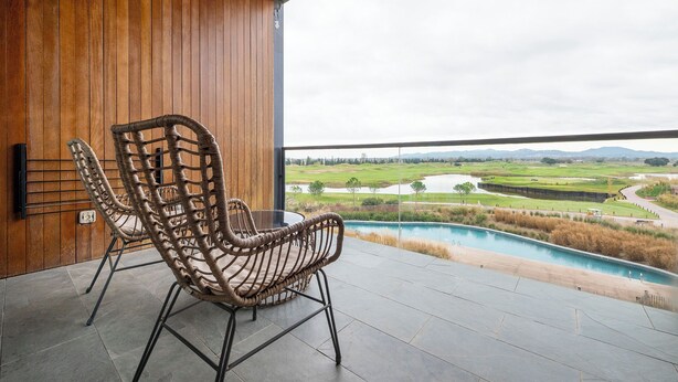 Una silla de mimbre en un balcón con vistas a un campo de golf y una piscina.