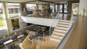 Interior de hotel con varios niveles, una escalera, zonas de estar y vistas al exterior.