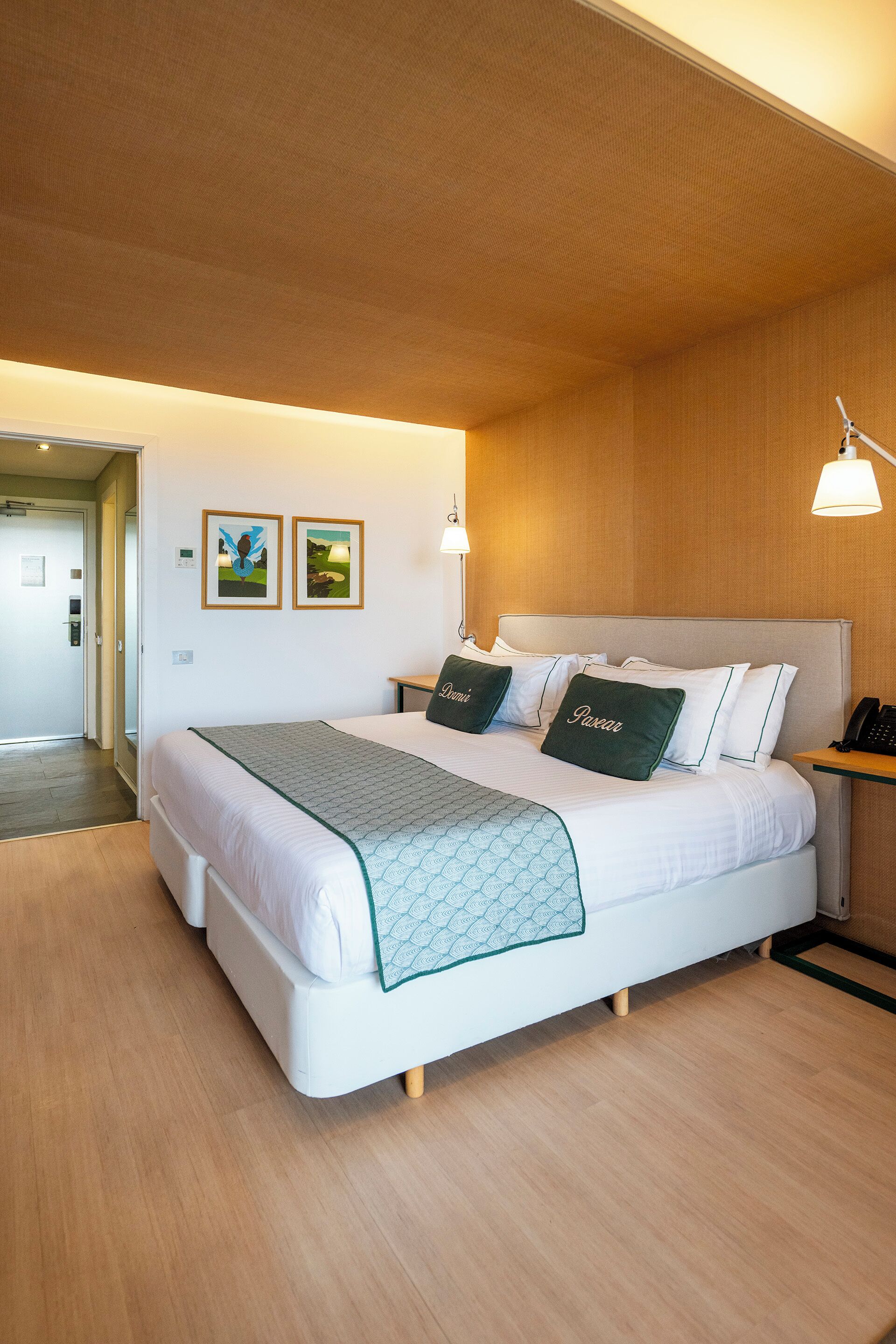 A hotel room with a large bed, a bedside table with a lamp, and two framed pictures on the wall.