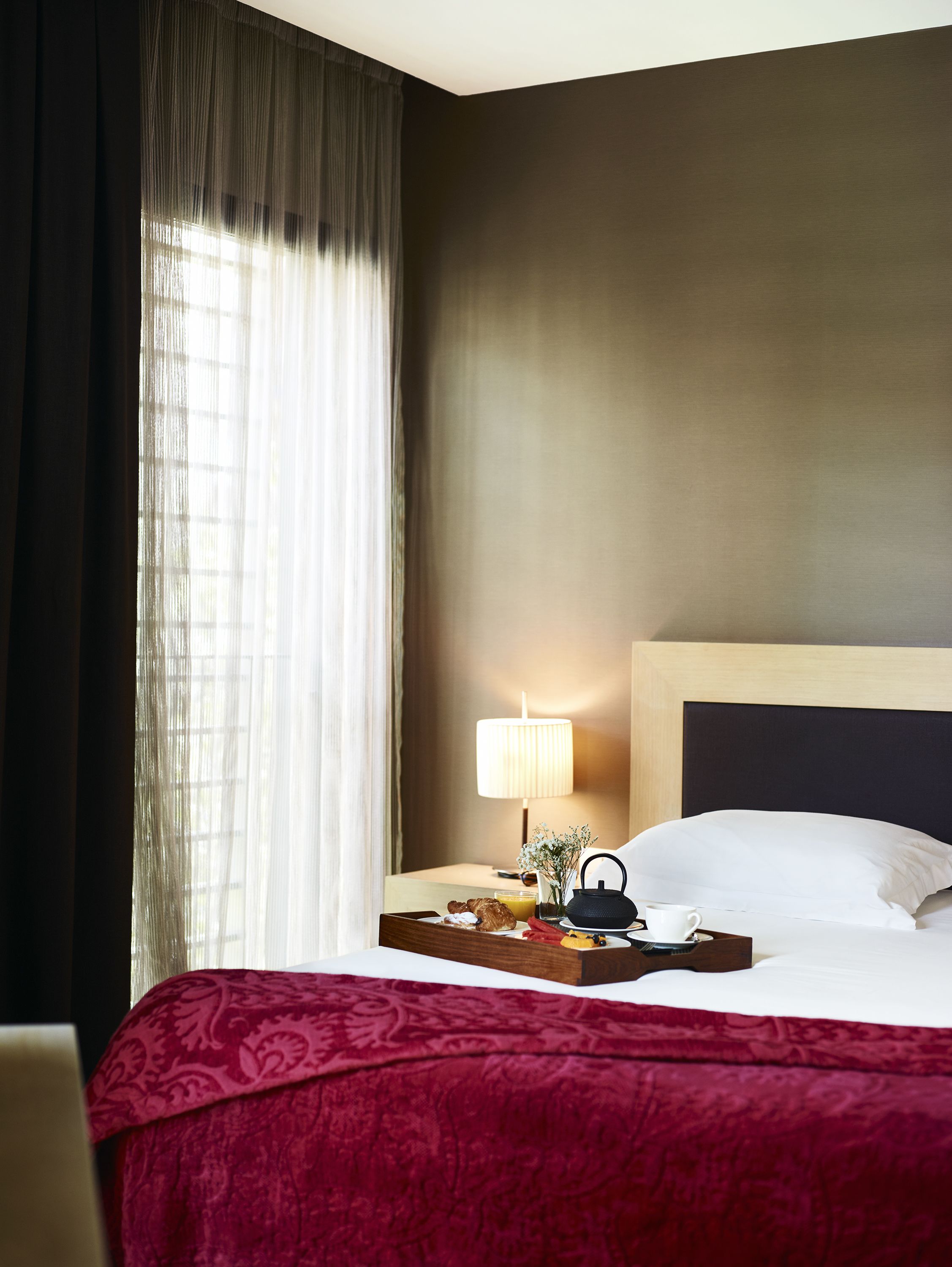 A hotel room with a large bed, a bedside table with a lamp, and a tray with breakfast items.