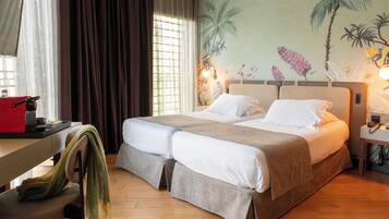 A double bed with a beige headboard, a desk with a red chair, and a wall with a tropical mural.