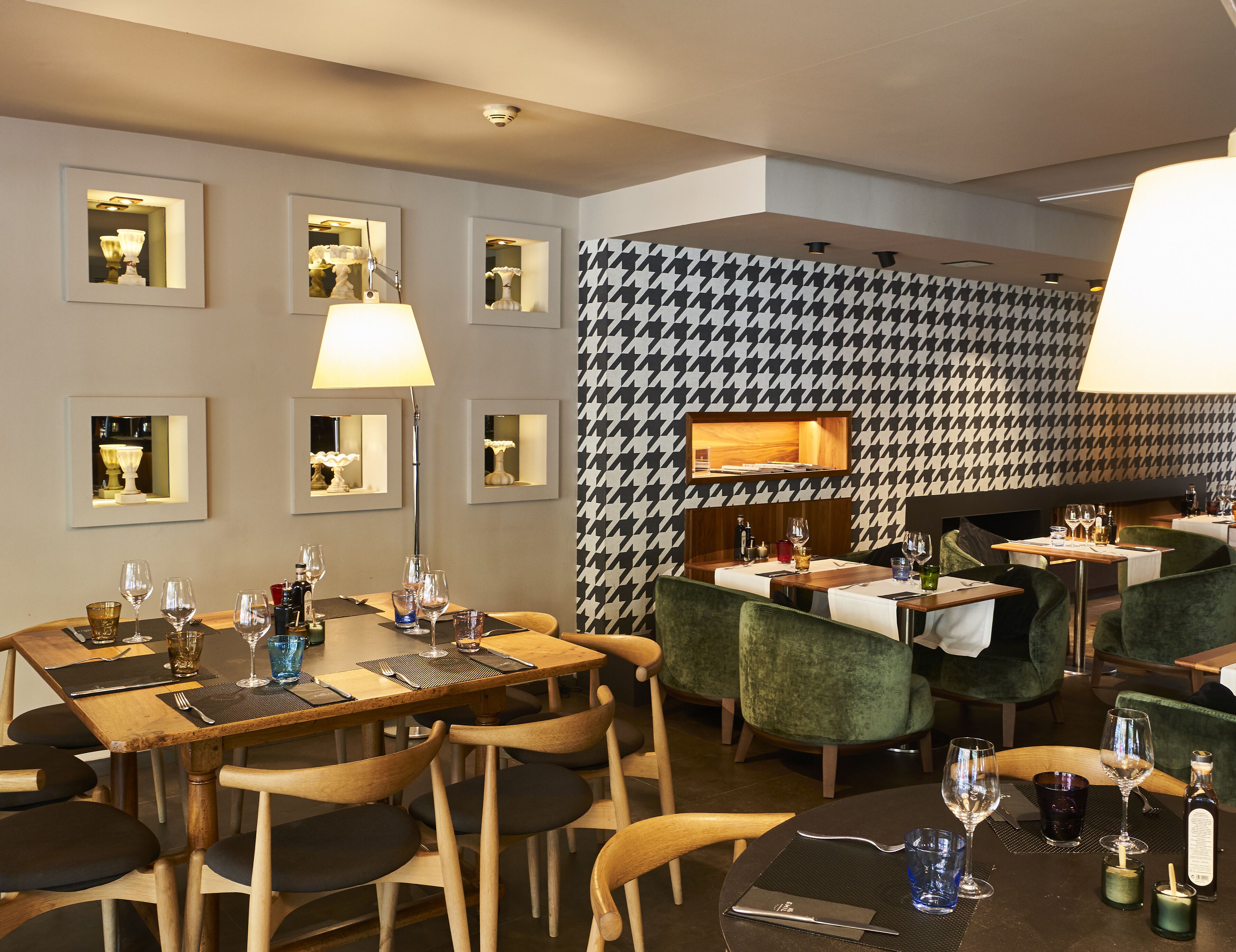 Un restaurant avec des tables et des chaises en bois, des miroirs encadrés aux murs et un mur orné d’un motif à carreaux.