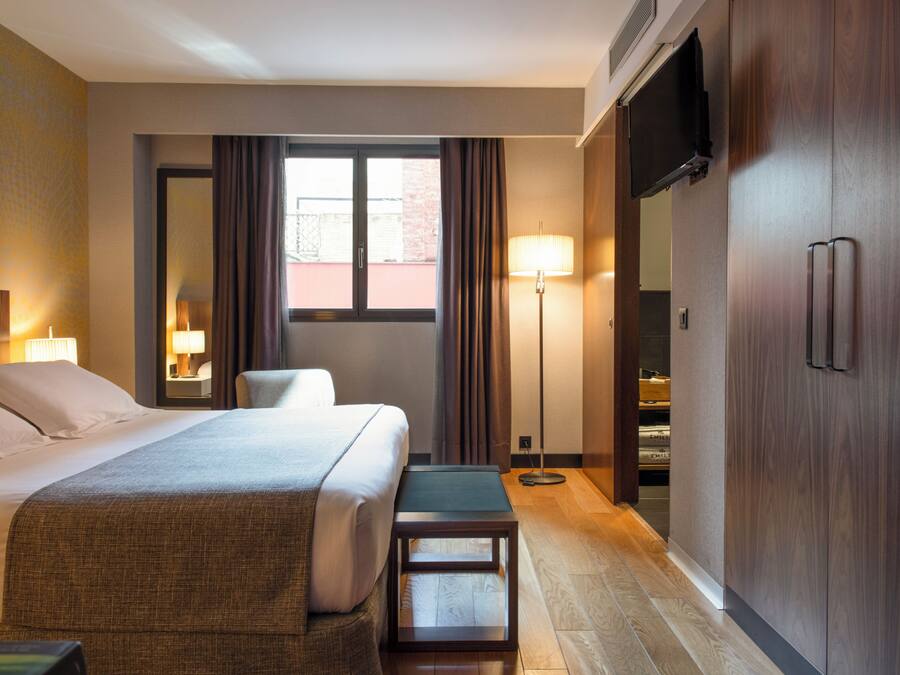 Habitación de hotel con una cama grande, lámparas de noche, escritorio, silla, lámpara de pie, armario y televisión.