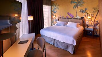 A hotel room with a bed, a desk, a chair, a TV, and a nightstand with a lamp.