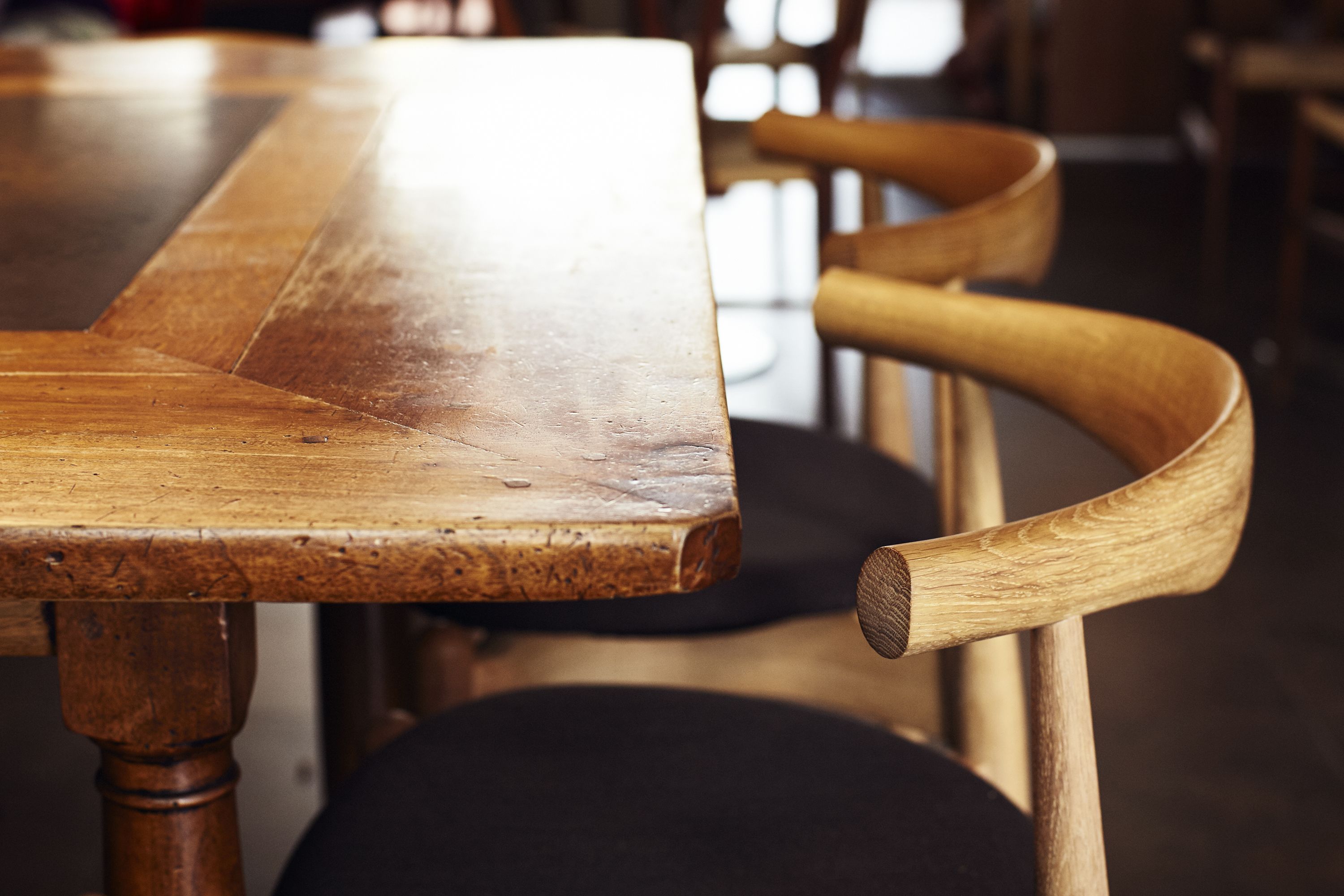 A wooden table with a polished surface and a curved wooden chair with a cushioned seat.