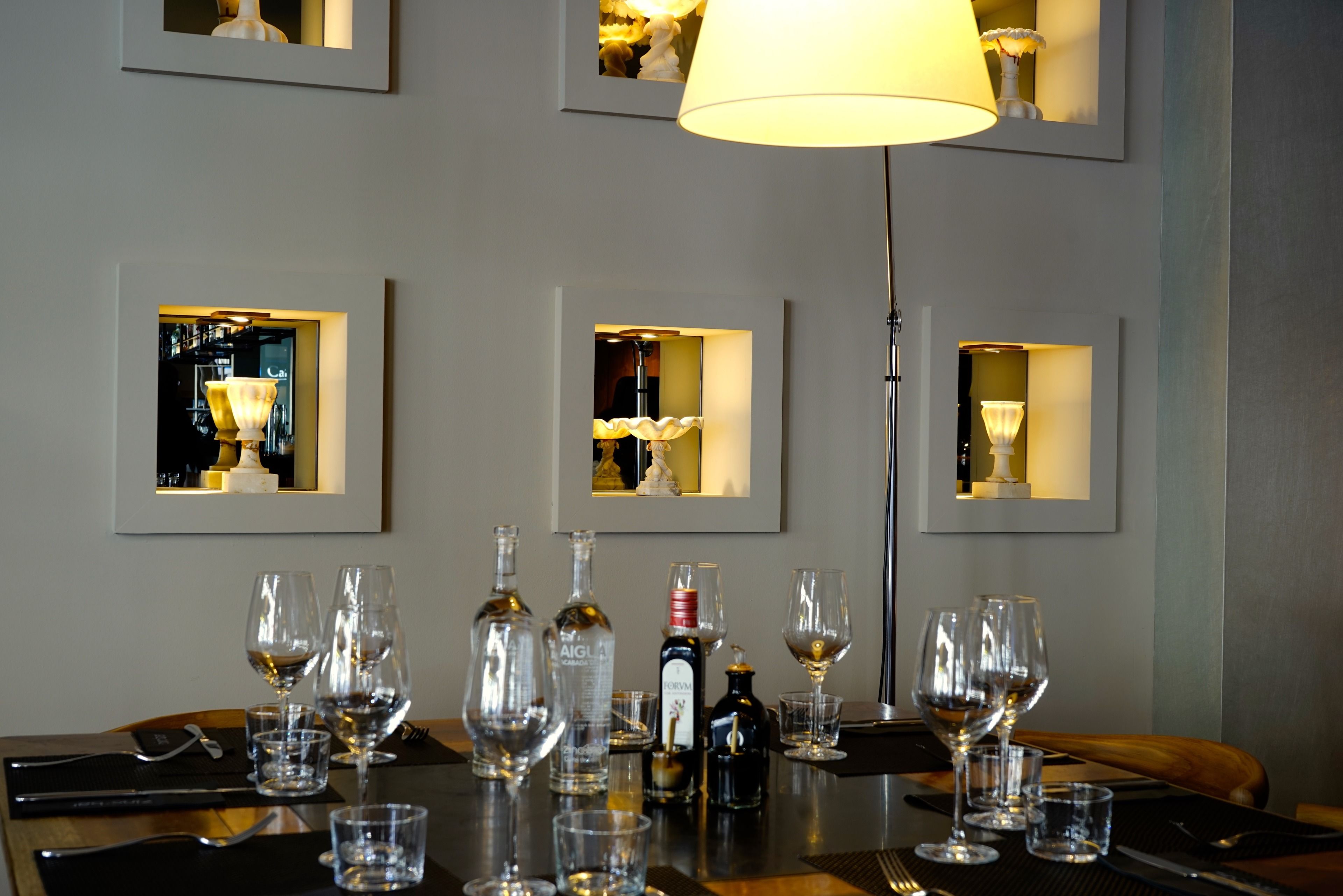 A dining table set with wine glasses, bottles, and cutlery, with framed pictures on the wall.