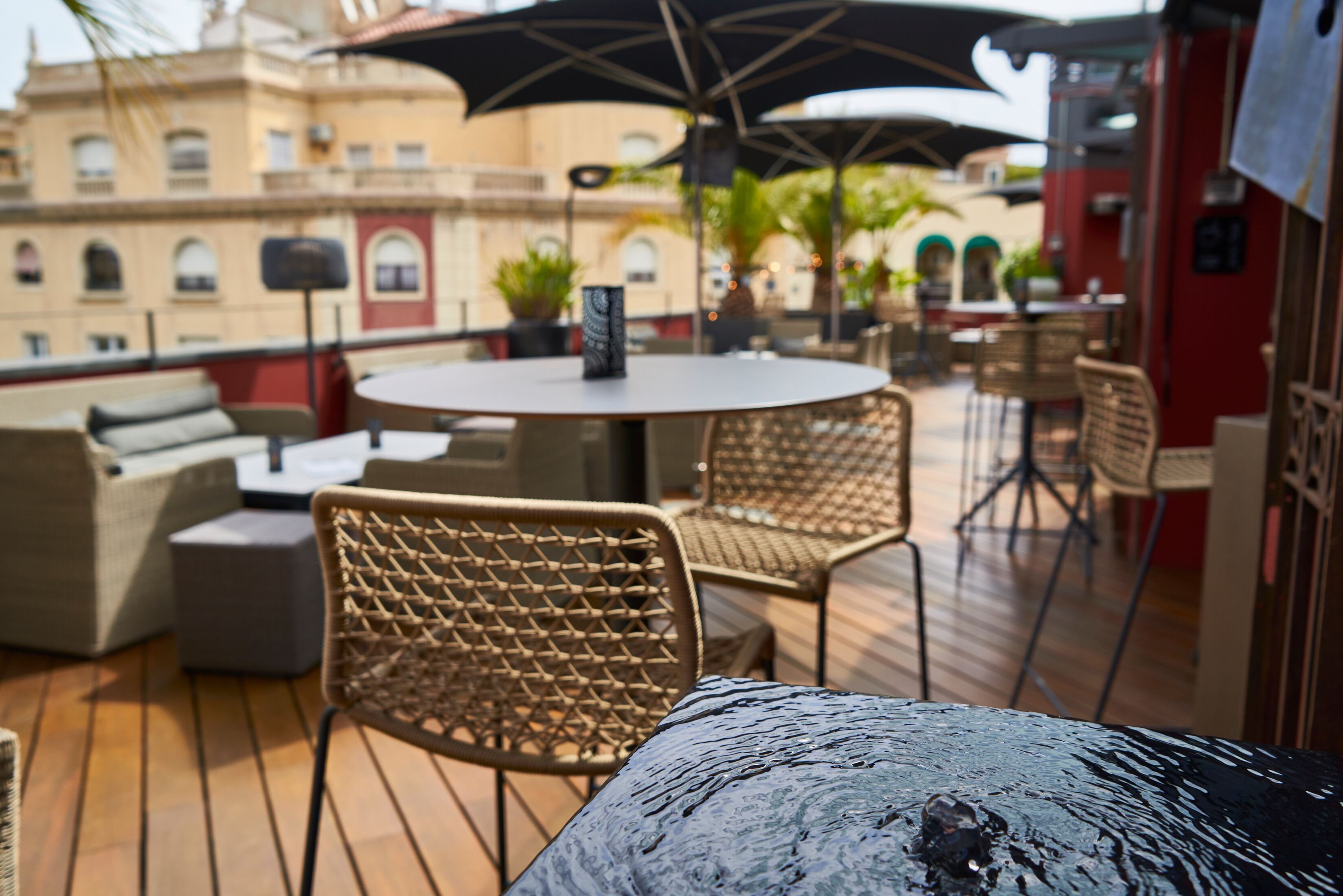 Una terraza con mobiliario de mimbre, una mesa redonda y sombrillas.