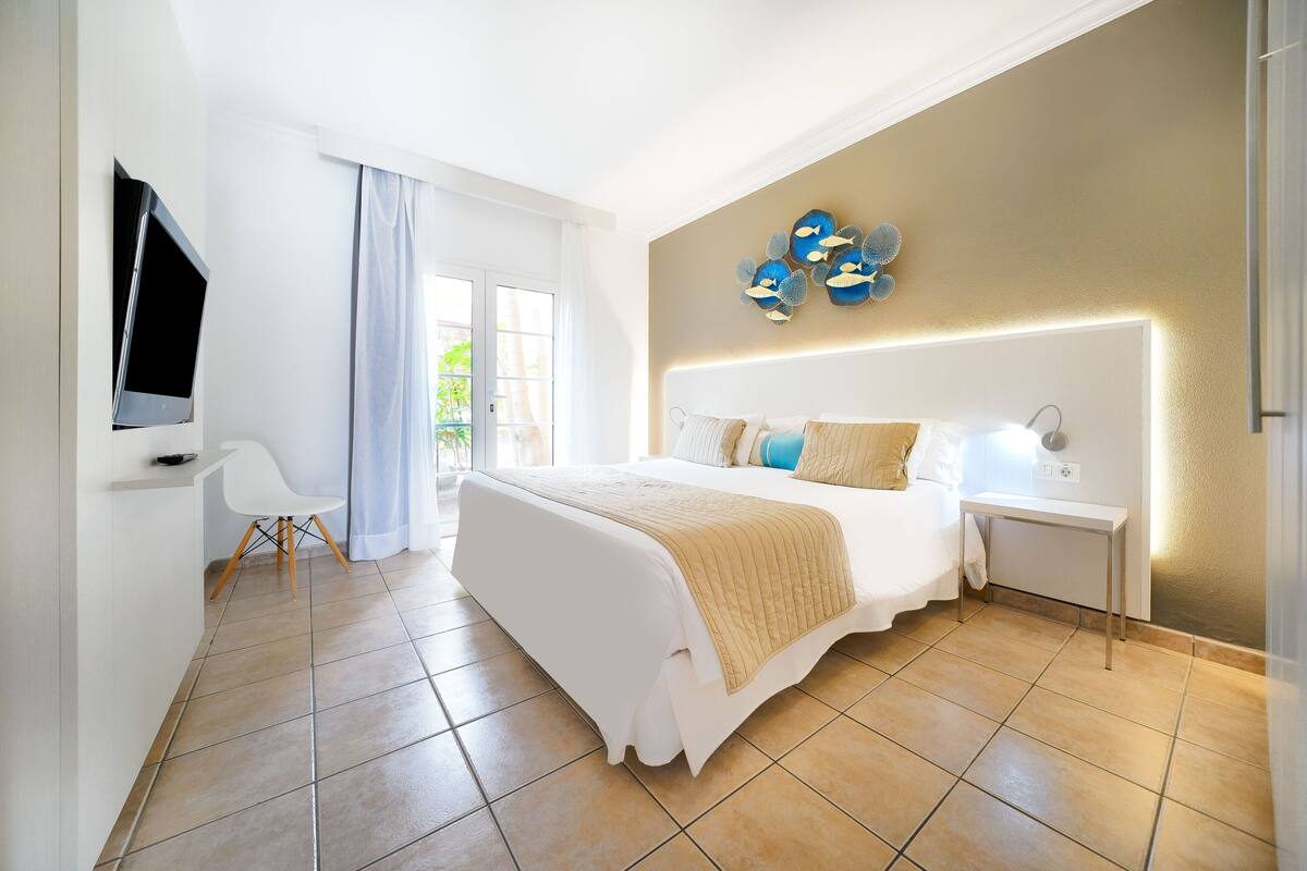 A modern bedroom with a large bed, bedside table, and a TV mounted on the wall.