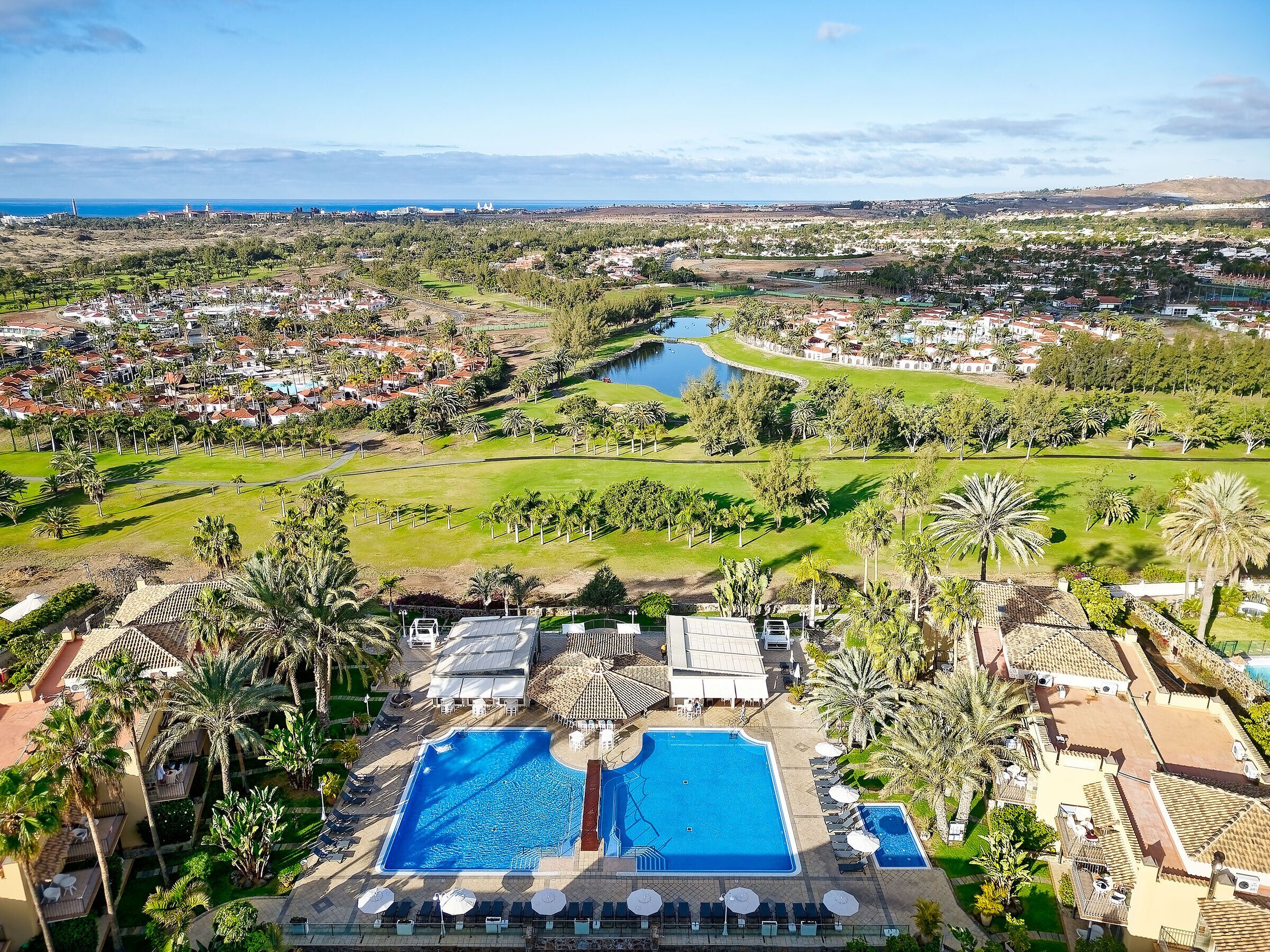 Ein Resort mit zwei großen Schwimmbecken, einem Golfplatz und Blick auf die umliegende Stadt.