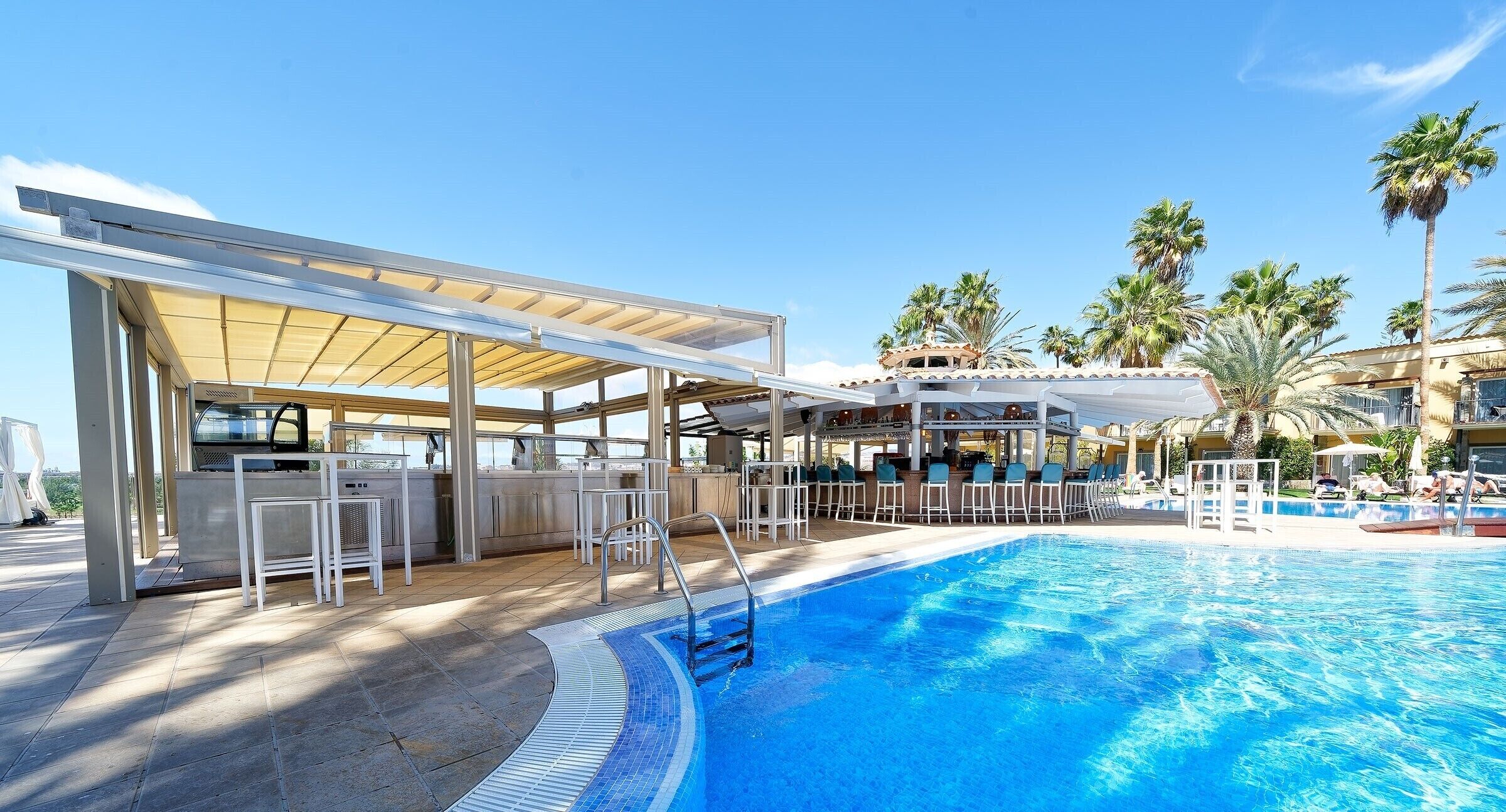 A swimming pool with a sunshade, lounge chairs, and a bar area.