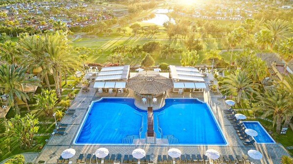 A large swimming pool with sun loungers and umbrellas, surrounded by palm trees and a view of a residential area. - Bull Vital Suites & Spa Boutique Hotel - Only Adults (San Bartolomé de Tirajana)