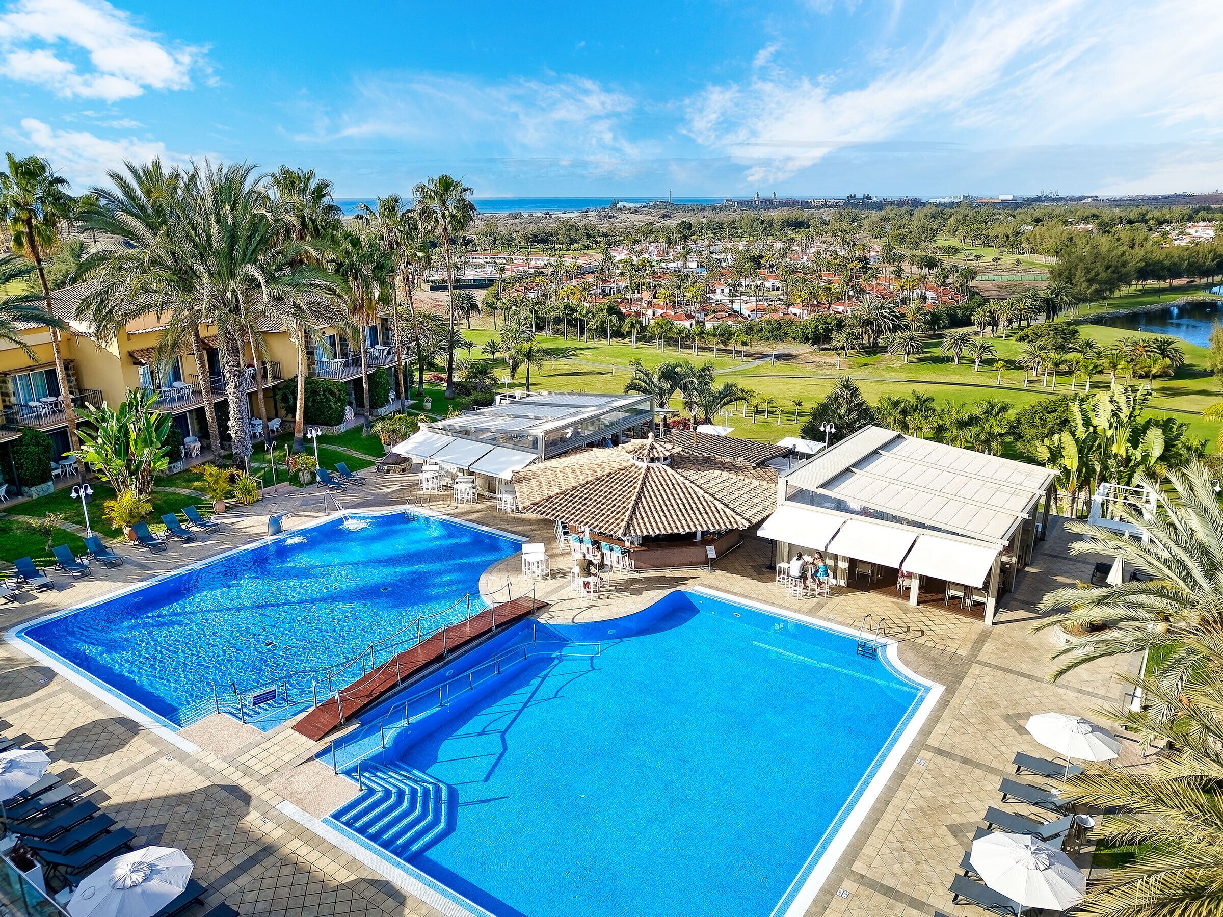 Un resort con una gran piscina, varias zonas de descanso y vistas del paisaje circundante.
