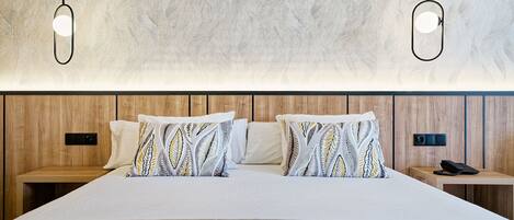 Ein Hotelzimmer mit einem großen Bett, gemusterten Kissen, einem Holzkopfende, Nachttischen und einem Telefon auf einem Tisch.