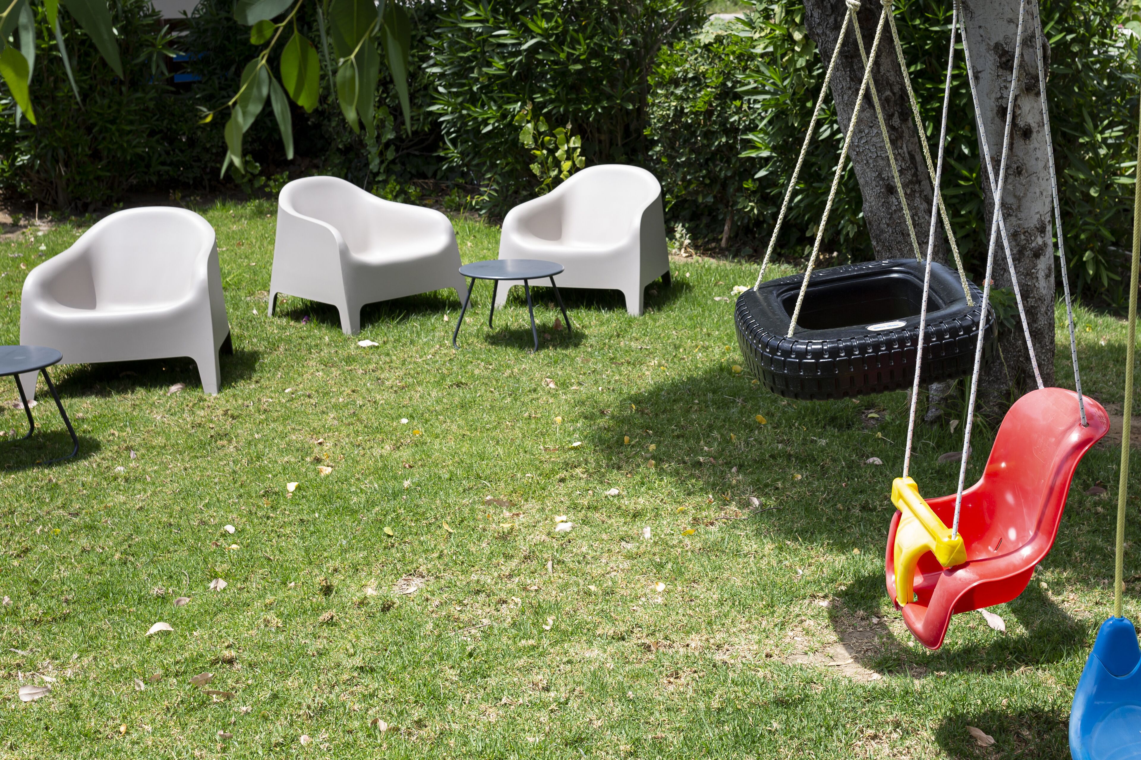 A grassy outdoor area with white plastic chairs and a small round table.