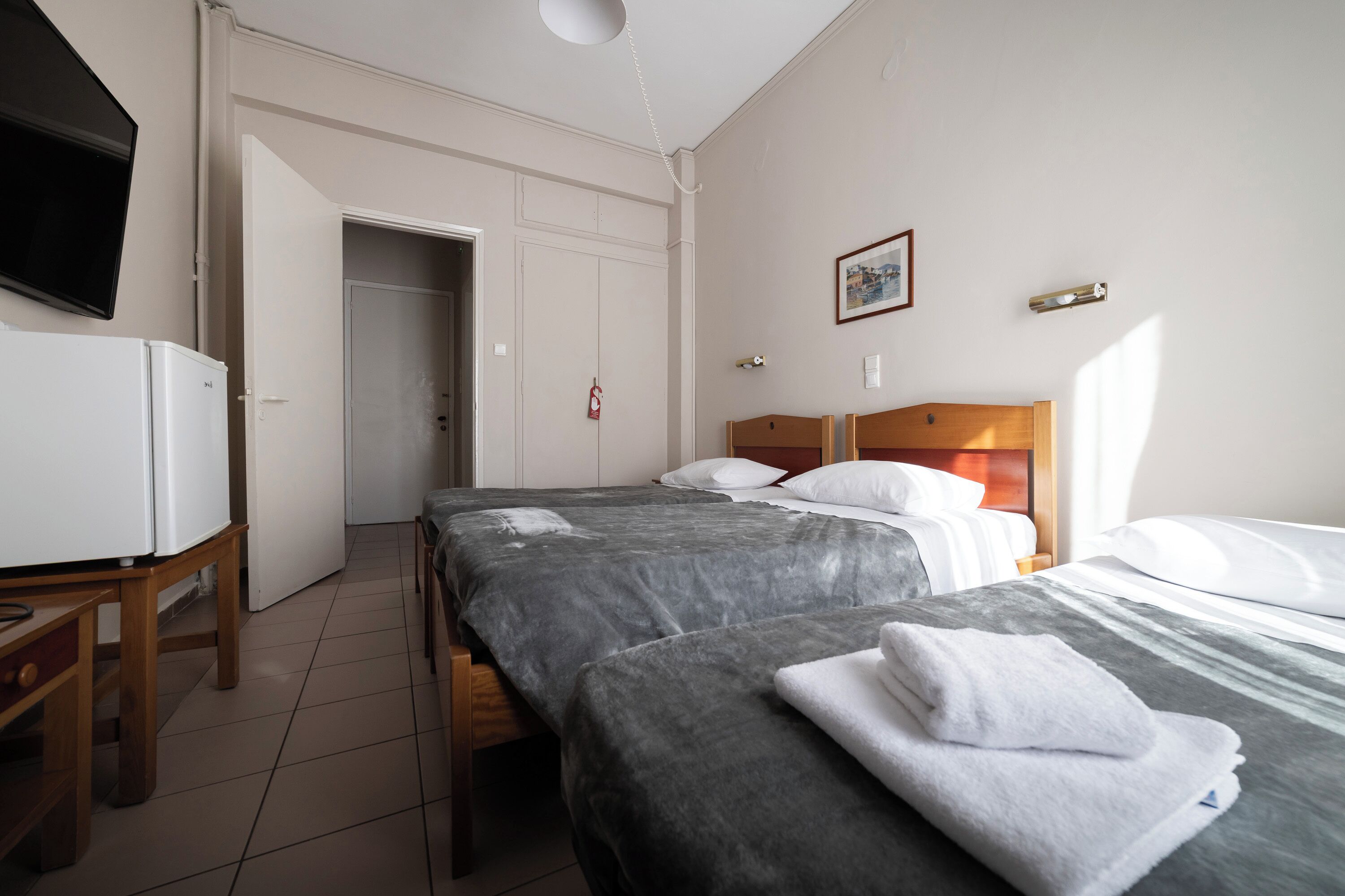 Quarto de hotel com duas camas, televisão, escrivaninha e porta que dá para um corredor.
