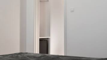 Een smalle gang met een kledingrek en een deur naar een kamer.