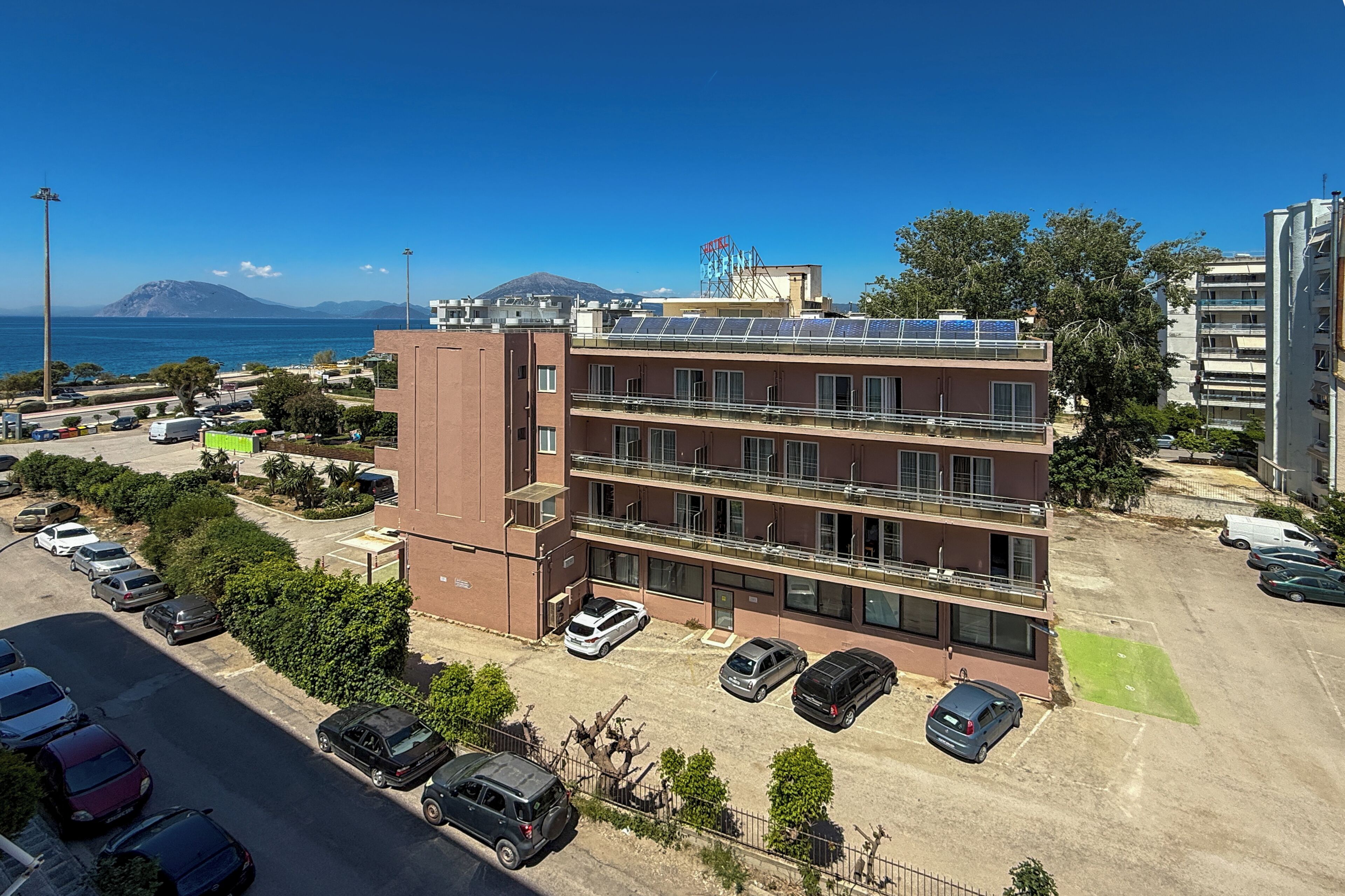 Un edificio de varios pisos con estacionamiento, vista al mar y una montaña al fondo.