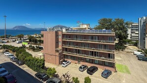 A multi-story building with a parking lot, a view of the sea, and a mountain in the background.
