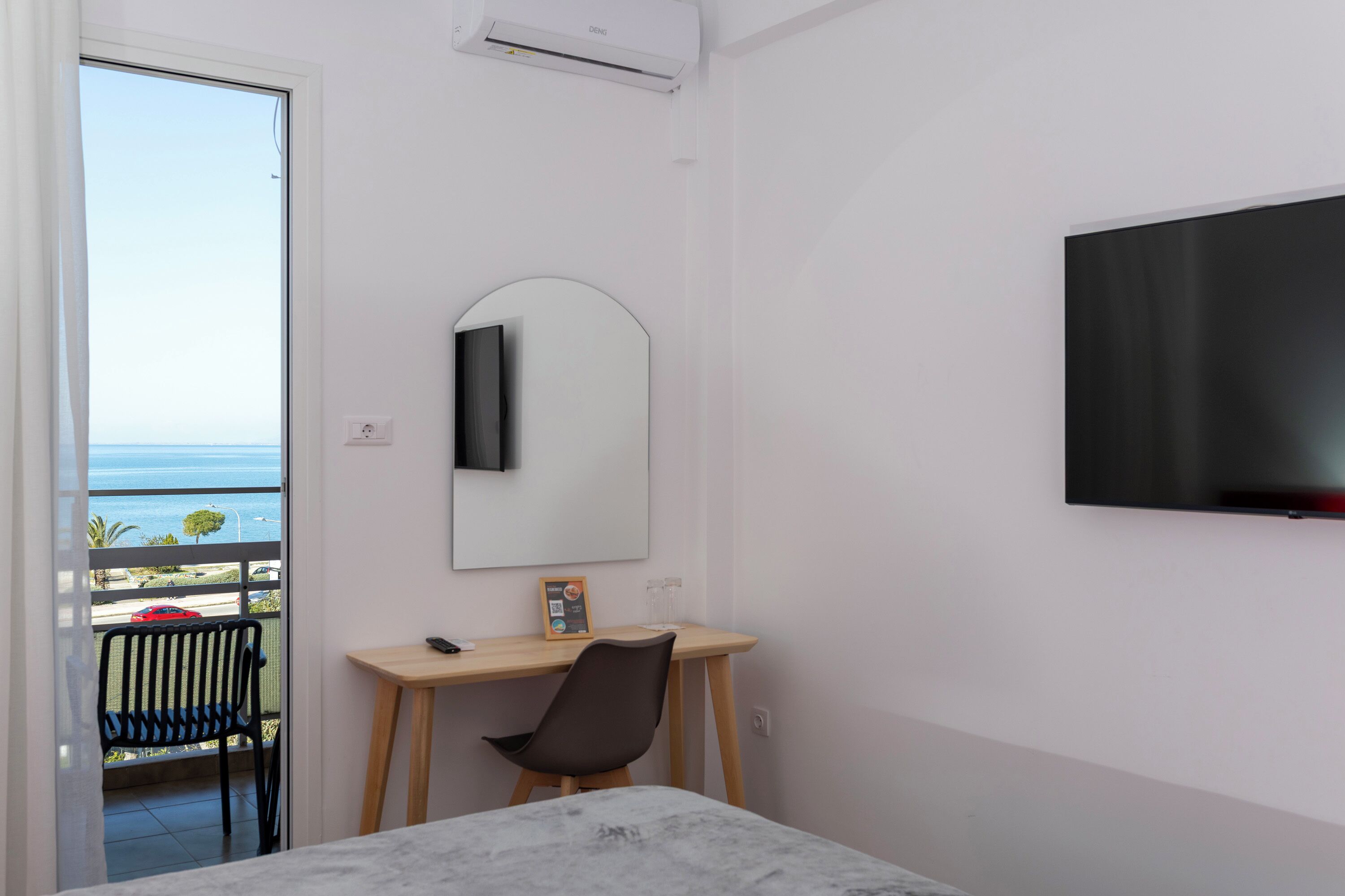 Habitación de hotel con cama, escritorio, silla, televisor, espejo y vista al mar.