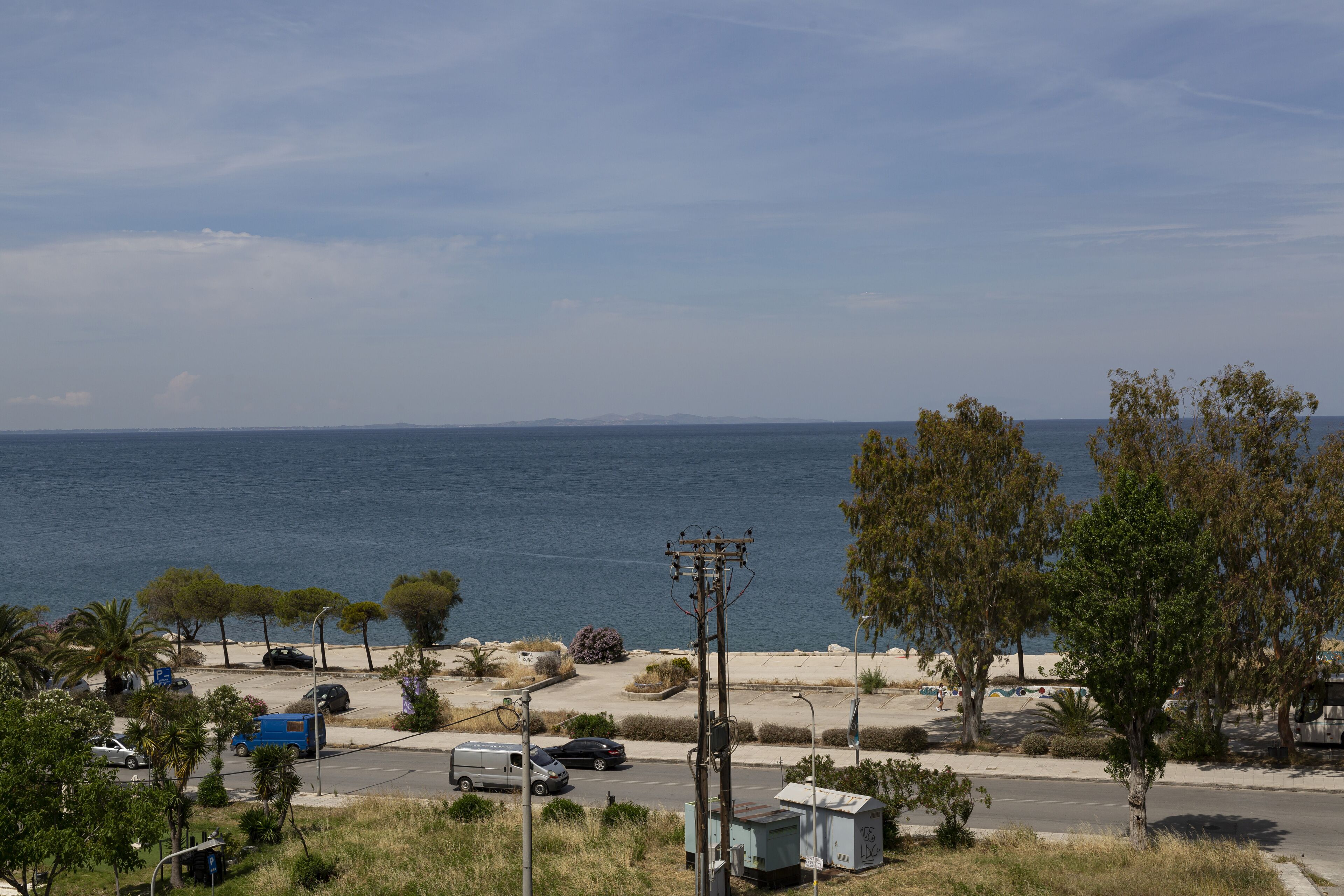 A coastal road with parked vehicles, a clear sky, and a view of the sea.