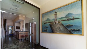 Un hall con un cuadro grande de un faro y barcos, una mesa de recepción y una escalera.