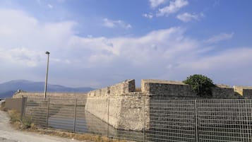 Eine historische Steinmauer mit einem Metallzaun im Vordergrund, eine Straßenlaterne und ein klarer Himmel.