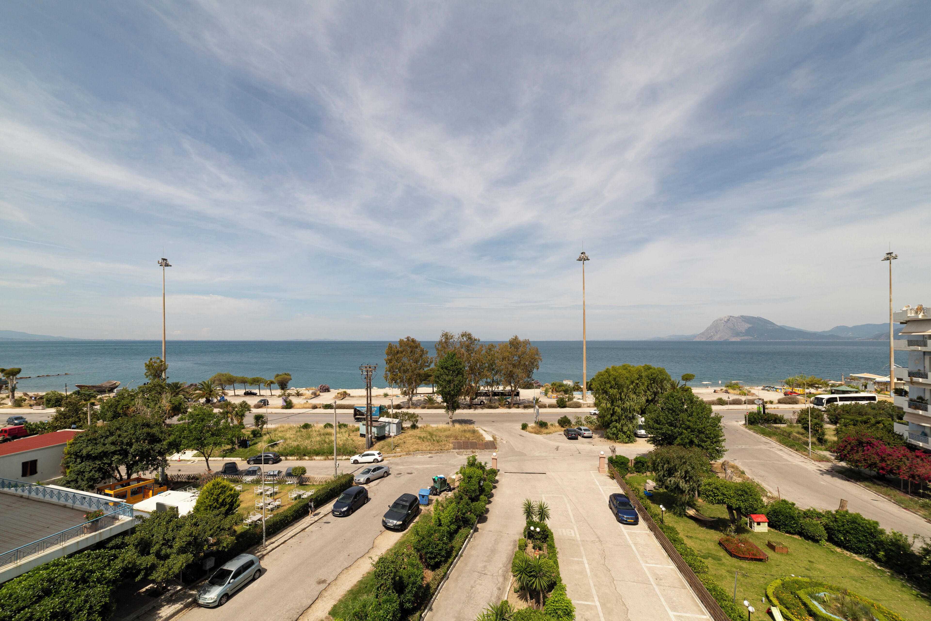 A parking lot with multiple cars, a road leading to a beach, and buildings in the background.