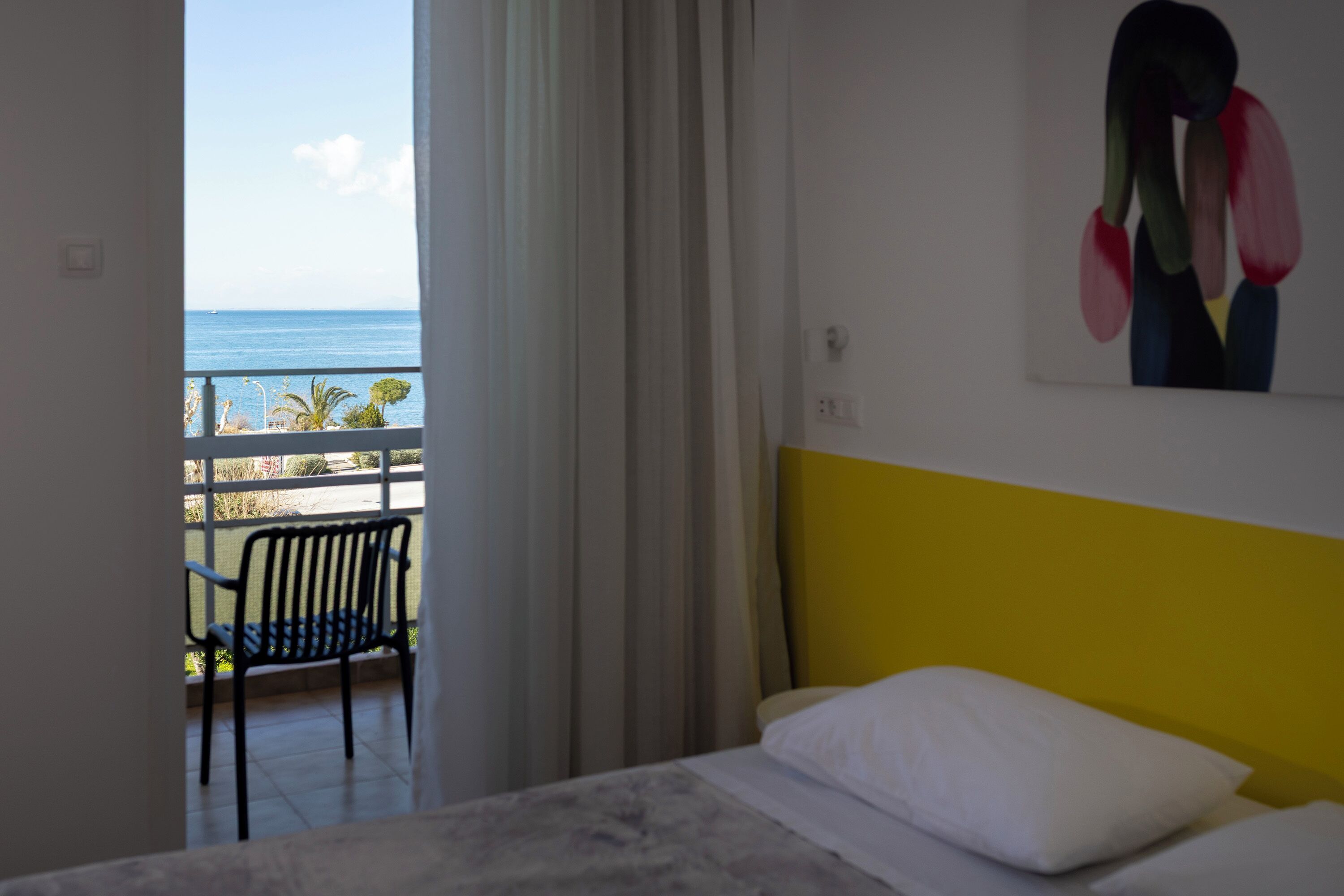 Una habitación con una cama, una silla, un cuadro y vistas al mar.