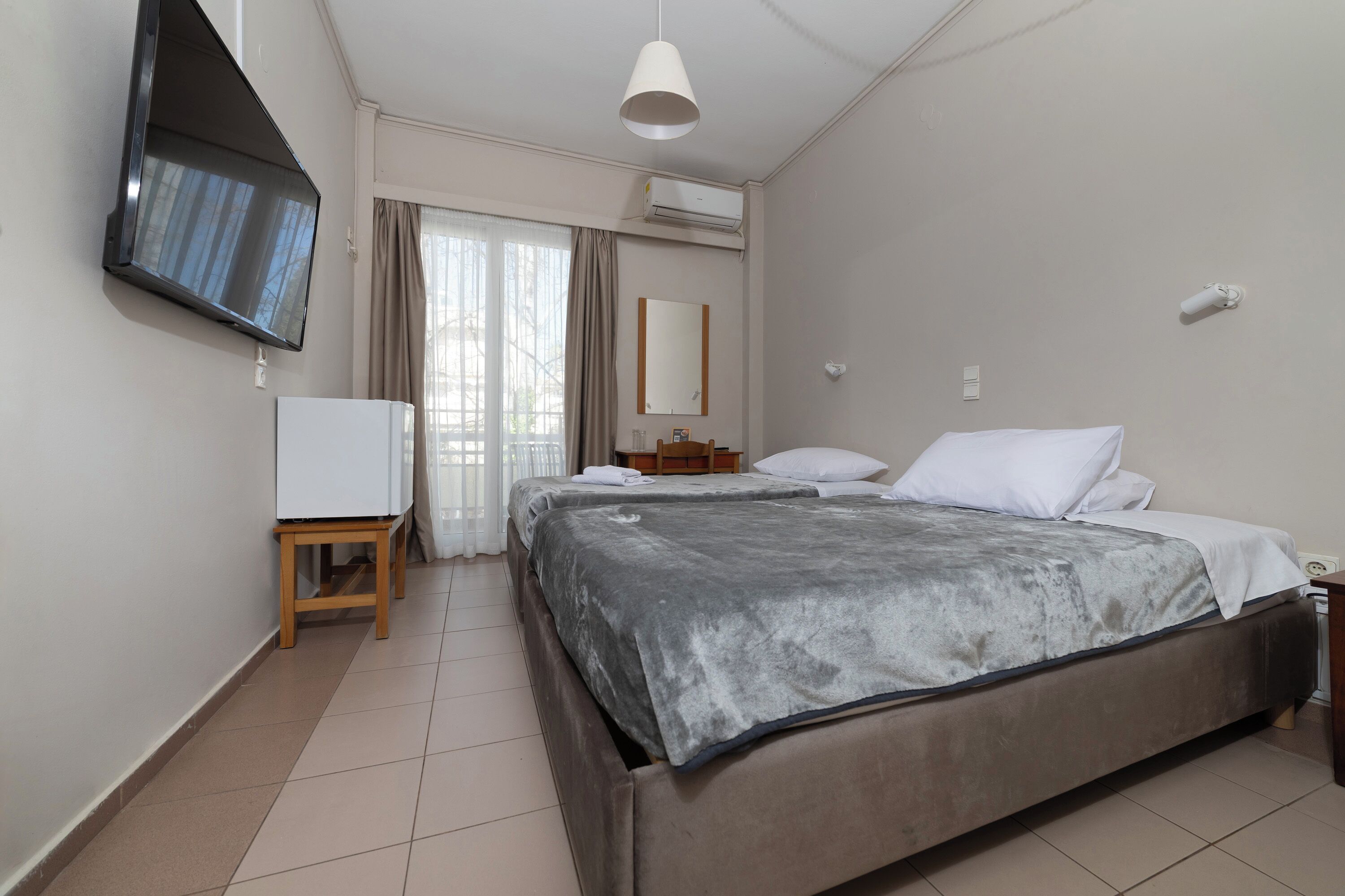 A hotel room with a bed, a TV mounted on the wall, a small table, and a window with curtains.