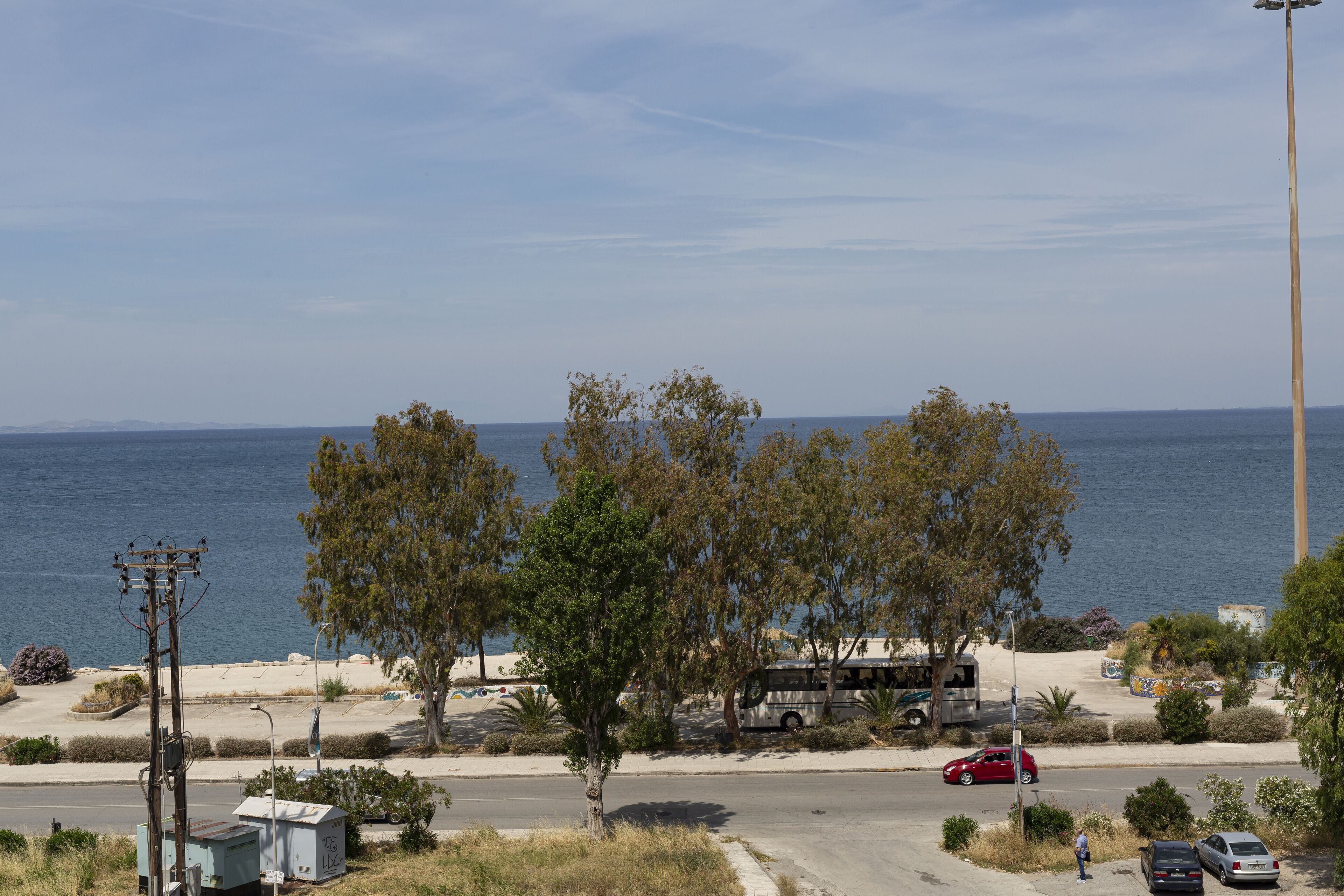 Eine Küstenstraße mit Strand im Hintergrund, ein Bus und parkende Autos.