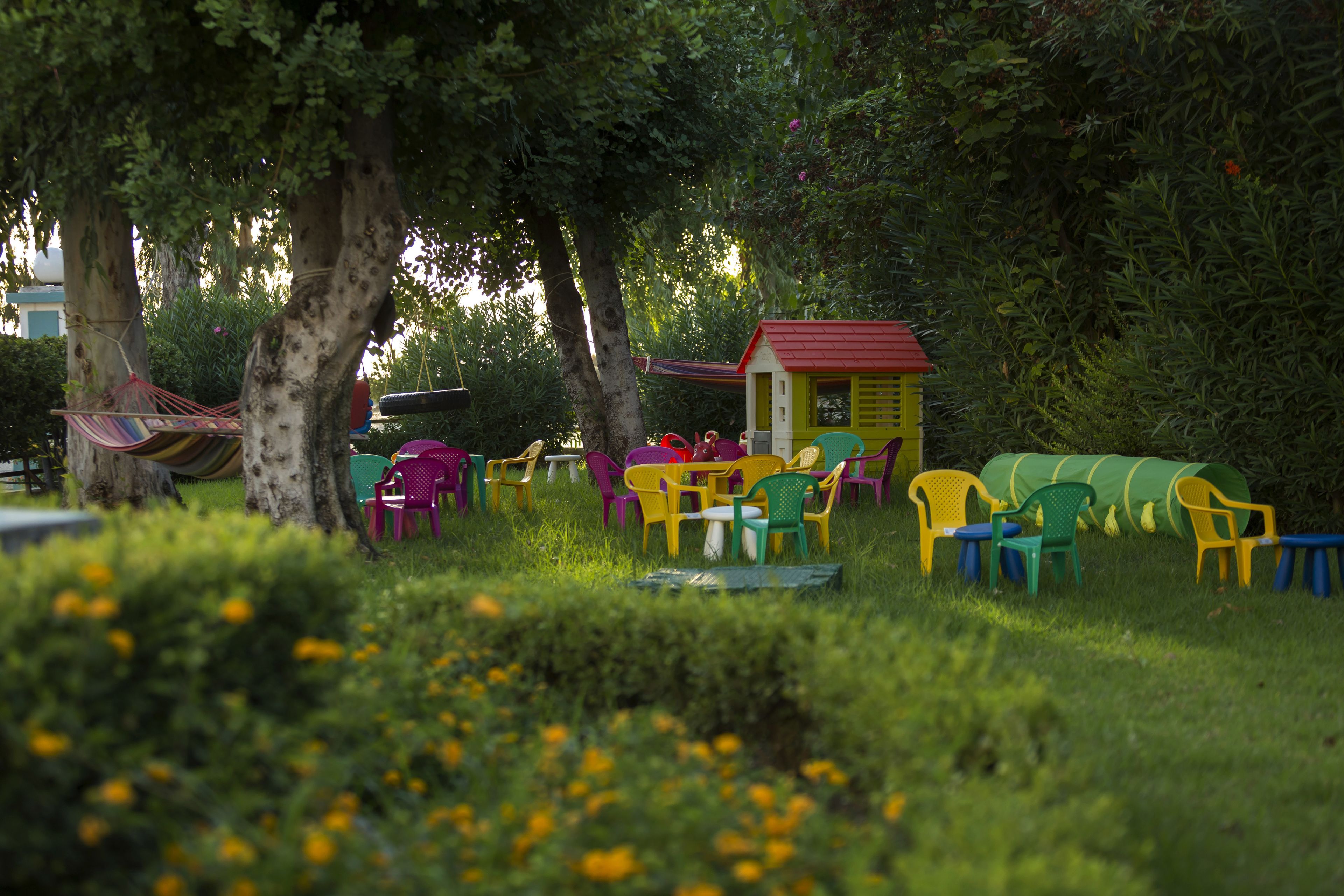 A garden with colorful plastic chairs and a small yellow building.