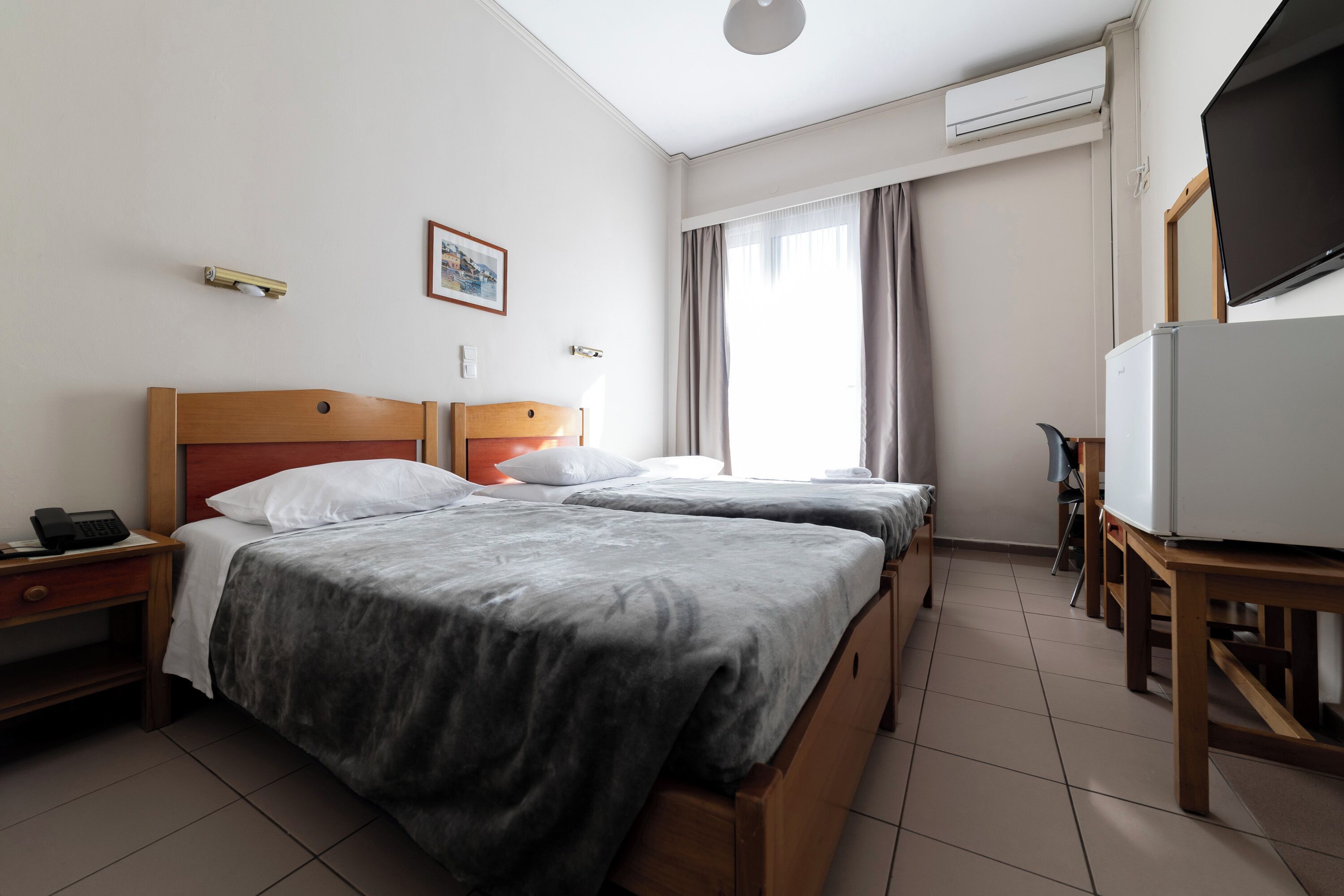 Habitación de hotel con dos camas, un escritorio, una silla, un televisor y un equipo de aire acondicionado.