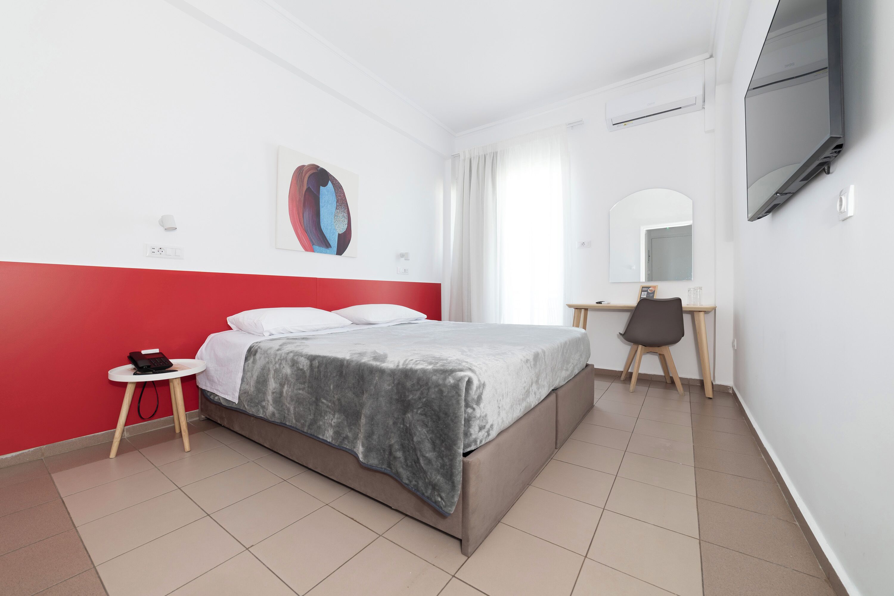 A hotel room with a bed, a desk, a chair, a TV, and a painting on the wall.