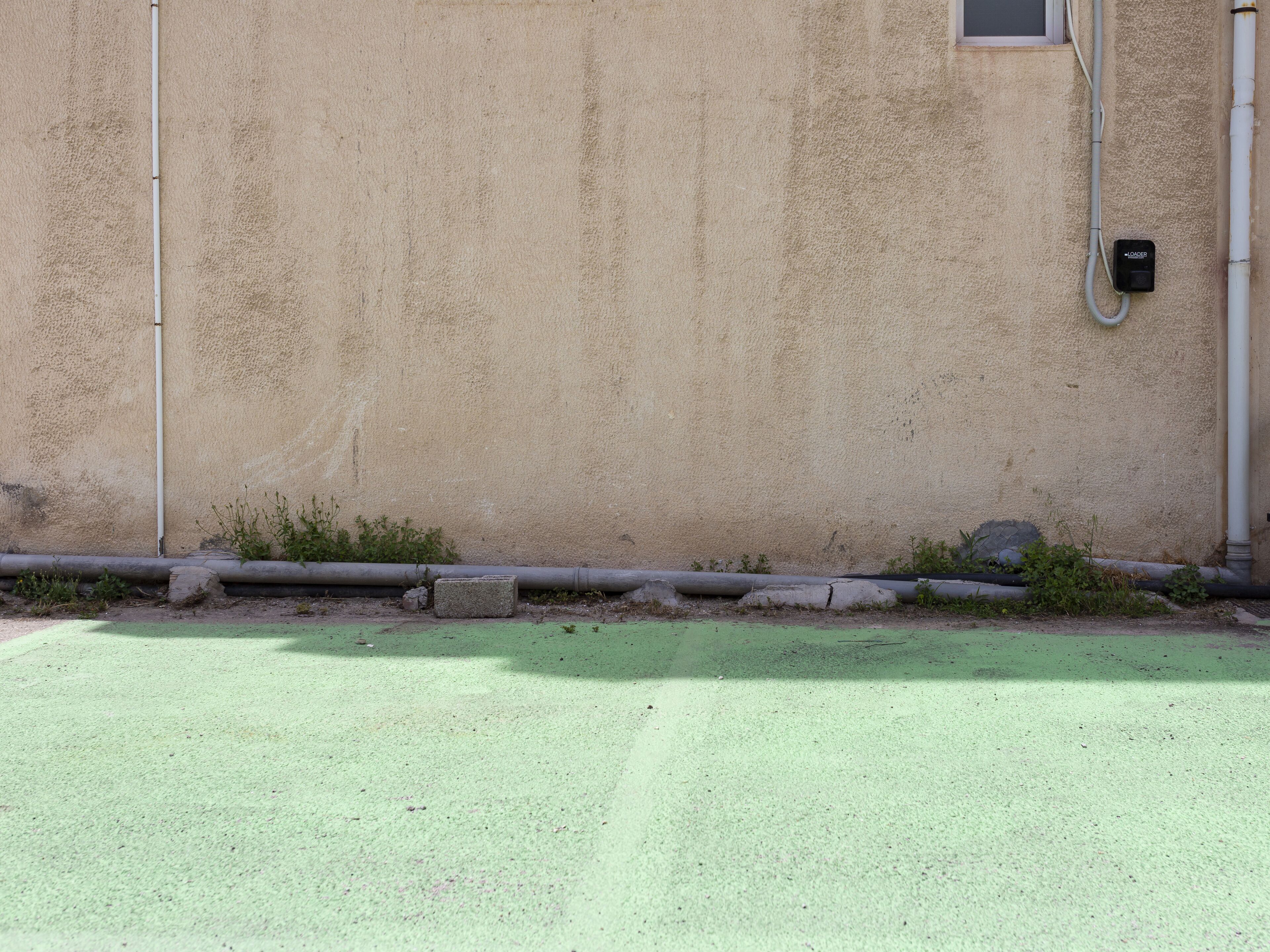 A building exterior with a textured beige wall, a window, and a green-painted ground.