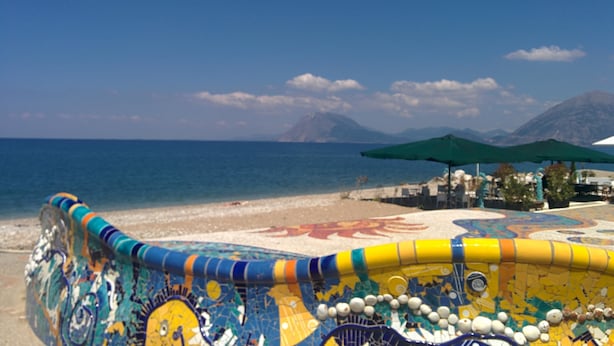 Una playa con coloridos diseños de mosaico, un cielo azul claro y montañas a lo lejos.