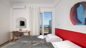 Un cuarto de hotel con cama, escritorio, silla, televisor, un cuadro y vista al mar.