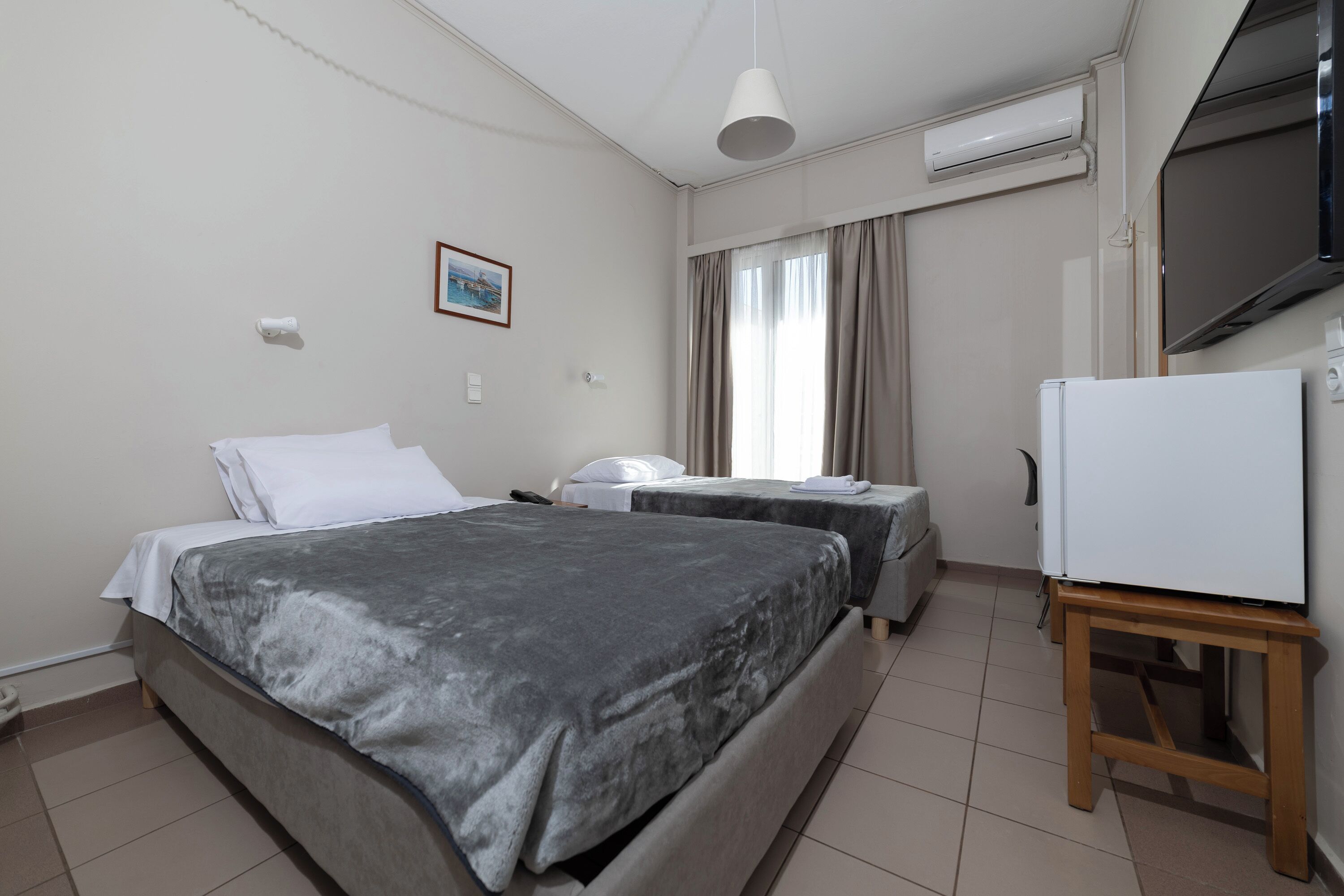 A hotel room with two beds, a TV, a refrigerator, and a window with curtains.
