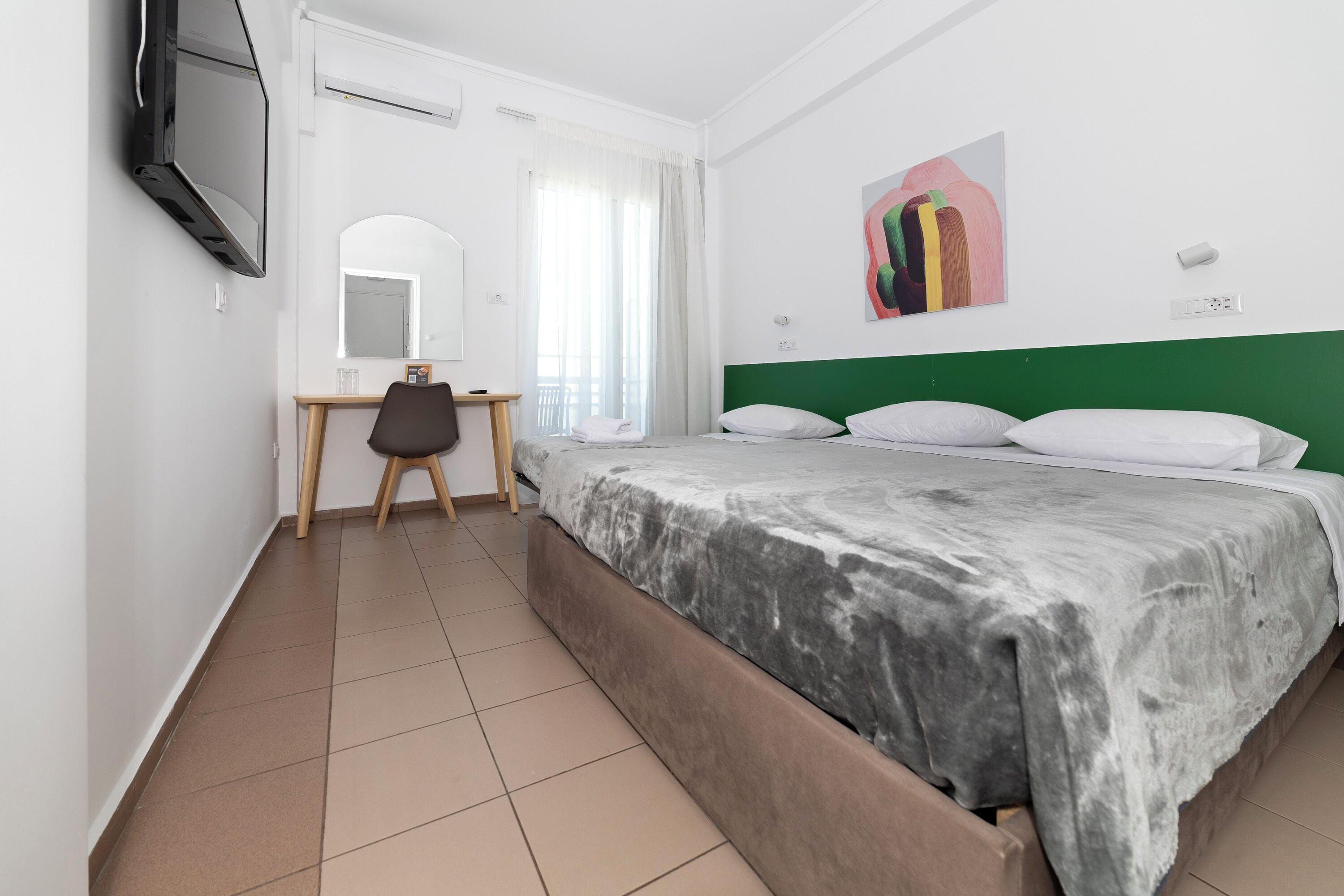 A hotel room with a bed, a desk, a chair, a TV, and a painting on the wall.