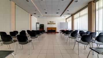 Un salón de conferencias con filas de sillas, un atril y un cartel que dice 'Hotel Delfini'.