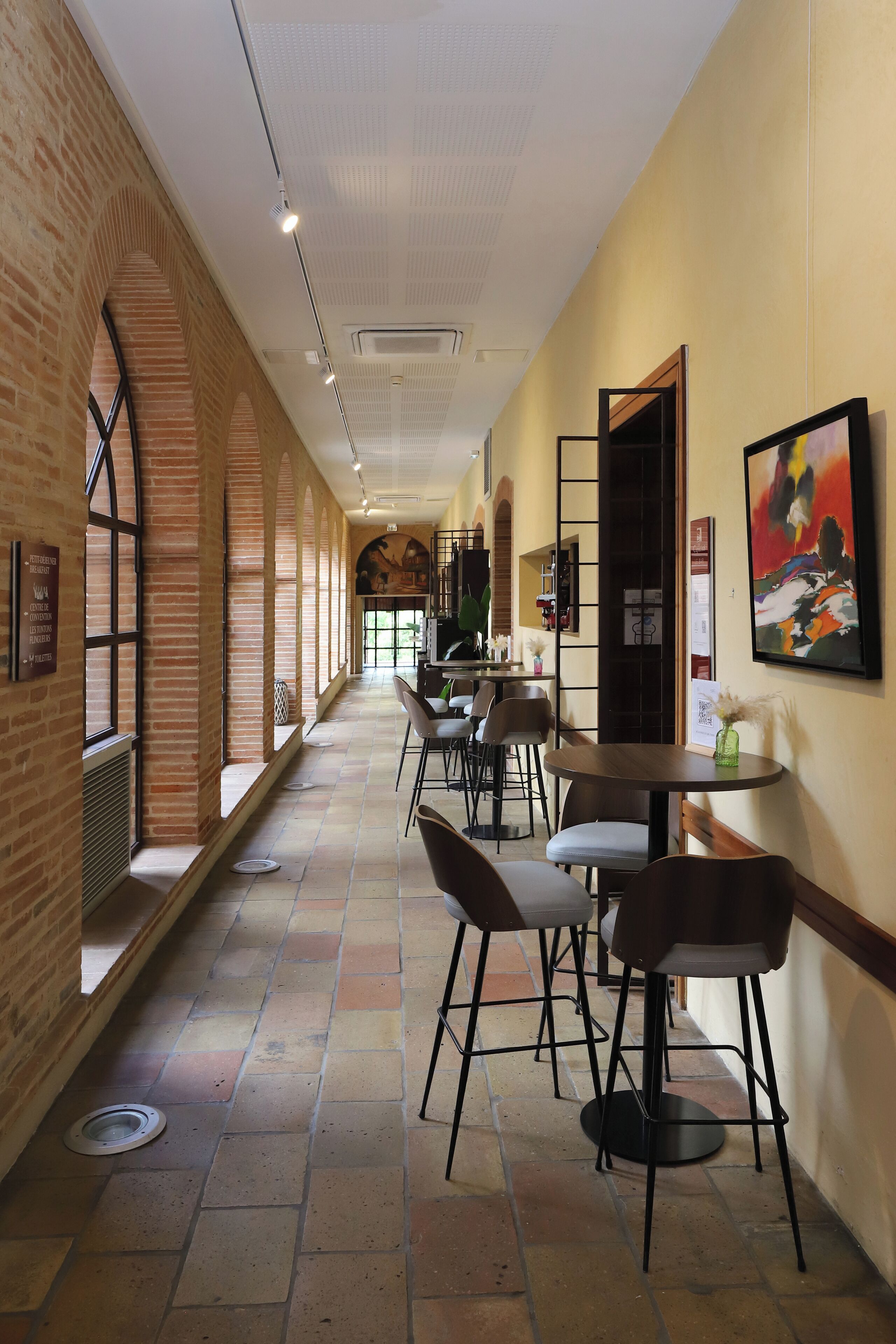 A corridor with brick walls, tiled flooring, and tables with chairs.