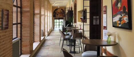 A corridor with brick walls, tiled flooring, and tables with chairs.
