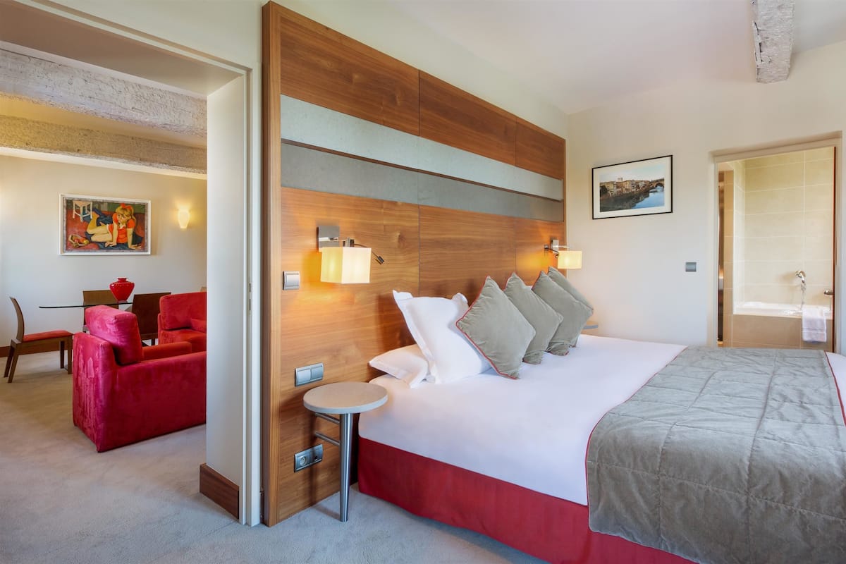 Quarto de hotel com uma cama grande, um sofá vermelho, uma mesa redonda pequena e uma cabeceira de madeira.